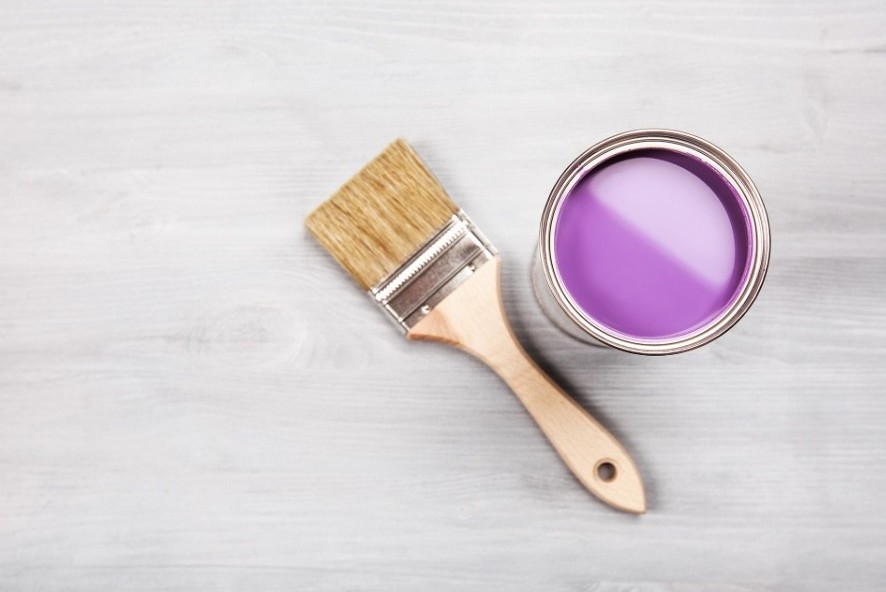 Lilla maling ved siden av en bred malepensel.